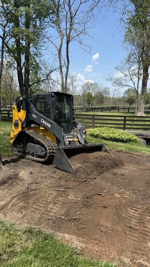 John Deere 317G grading and leveling a dirt site in a fenced pasture