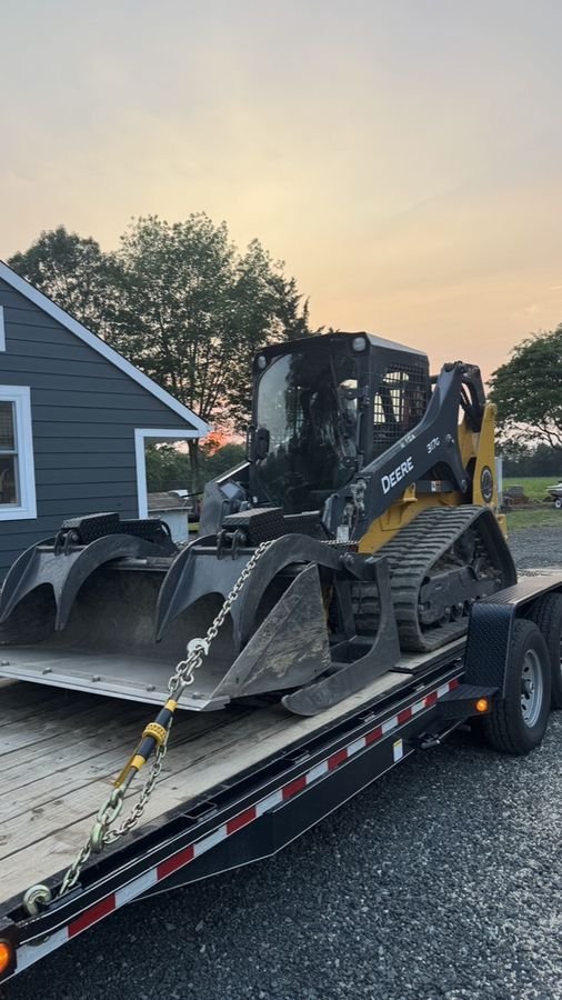 John Deere 317G loaded on a trailer with grapple attachment for delivery